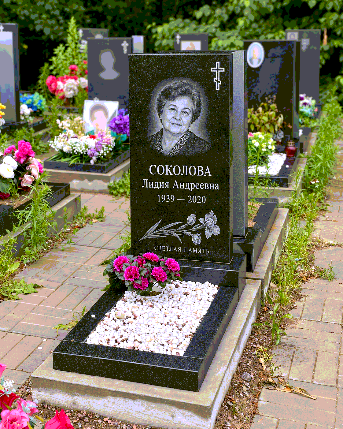 Памятник со светлым камнем в цветнике после установки на участке. Имена, даты и портреты изменены.