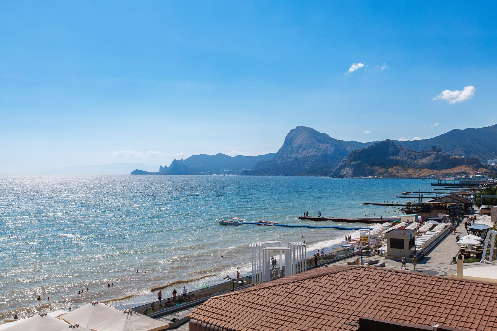 Sunlit coastline with beach promenade, mountains and the blue sea