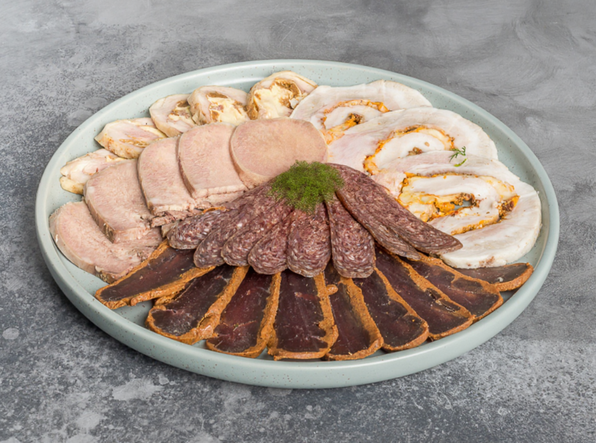 Мясное ассорти: нарезка ветчины и колбас с зеленью на круглой тарелке