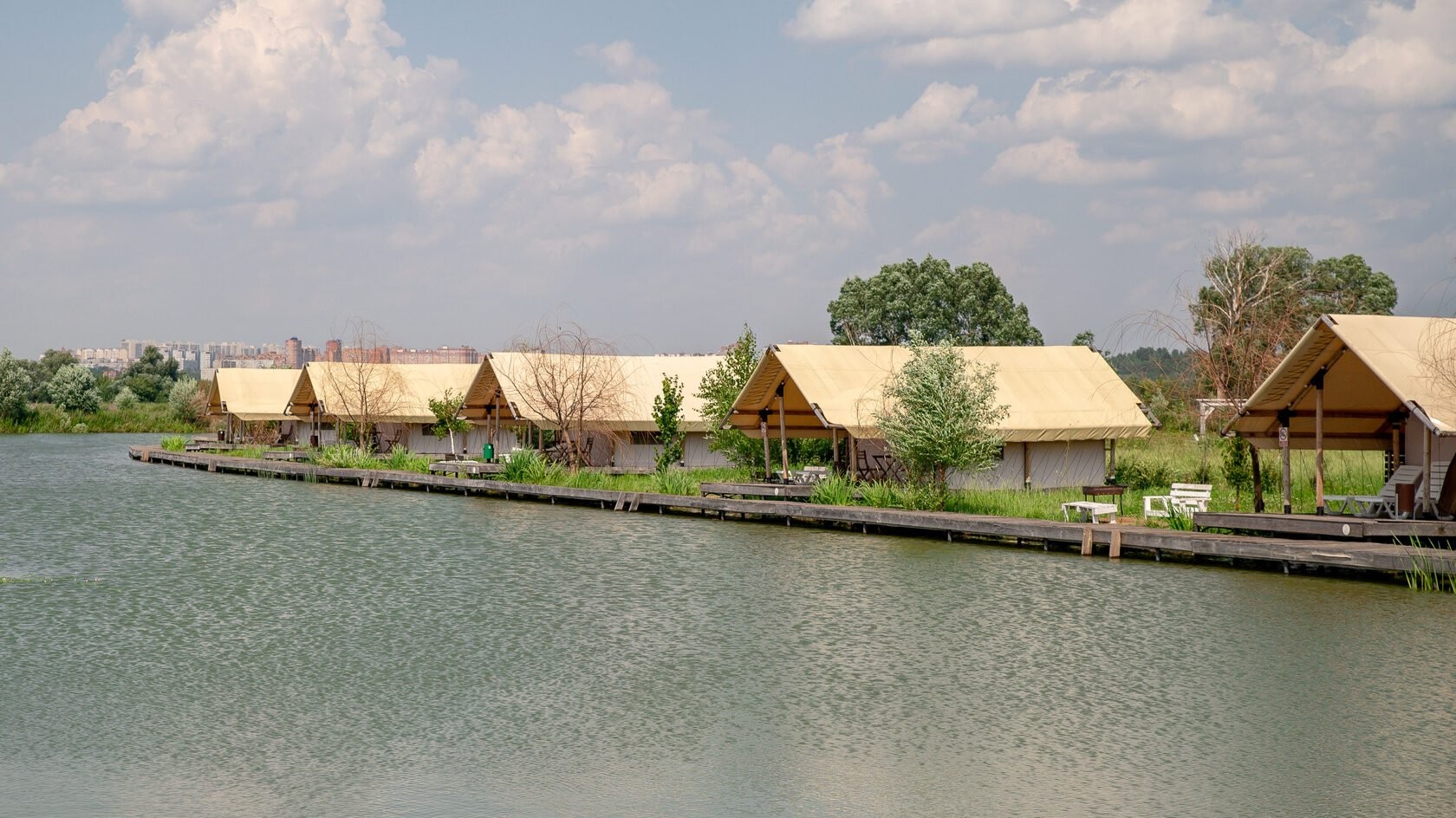 A row of safari tents on the boardwalk along the water at Ostrov Glamping