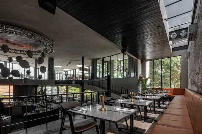 A modern, luxurious two-story space with industrial elements, large windows, and sleek dining tables at Hedonist Uluwatu, a high-end choice for the best shisha lounge in Bali.