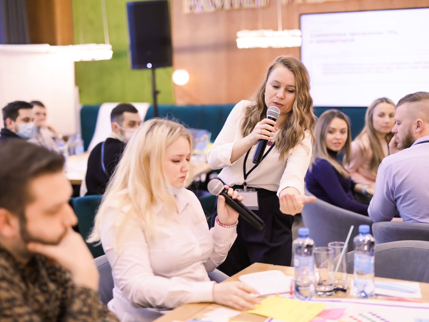 Модератор передаёт микрофон участнику во время групповой работы на воркшопе