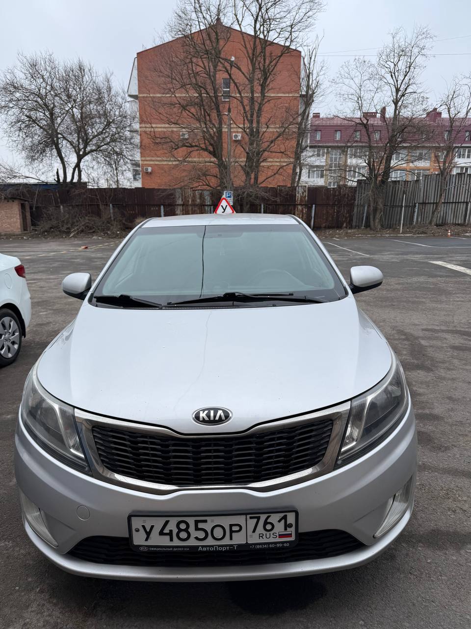 Серебристый учебный Kia Rio на площадке перед домом