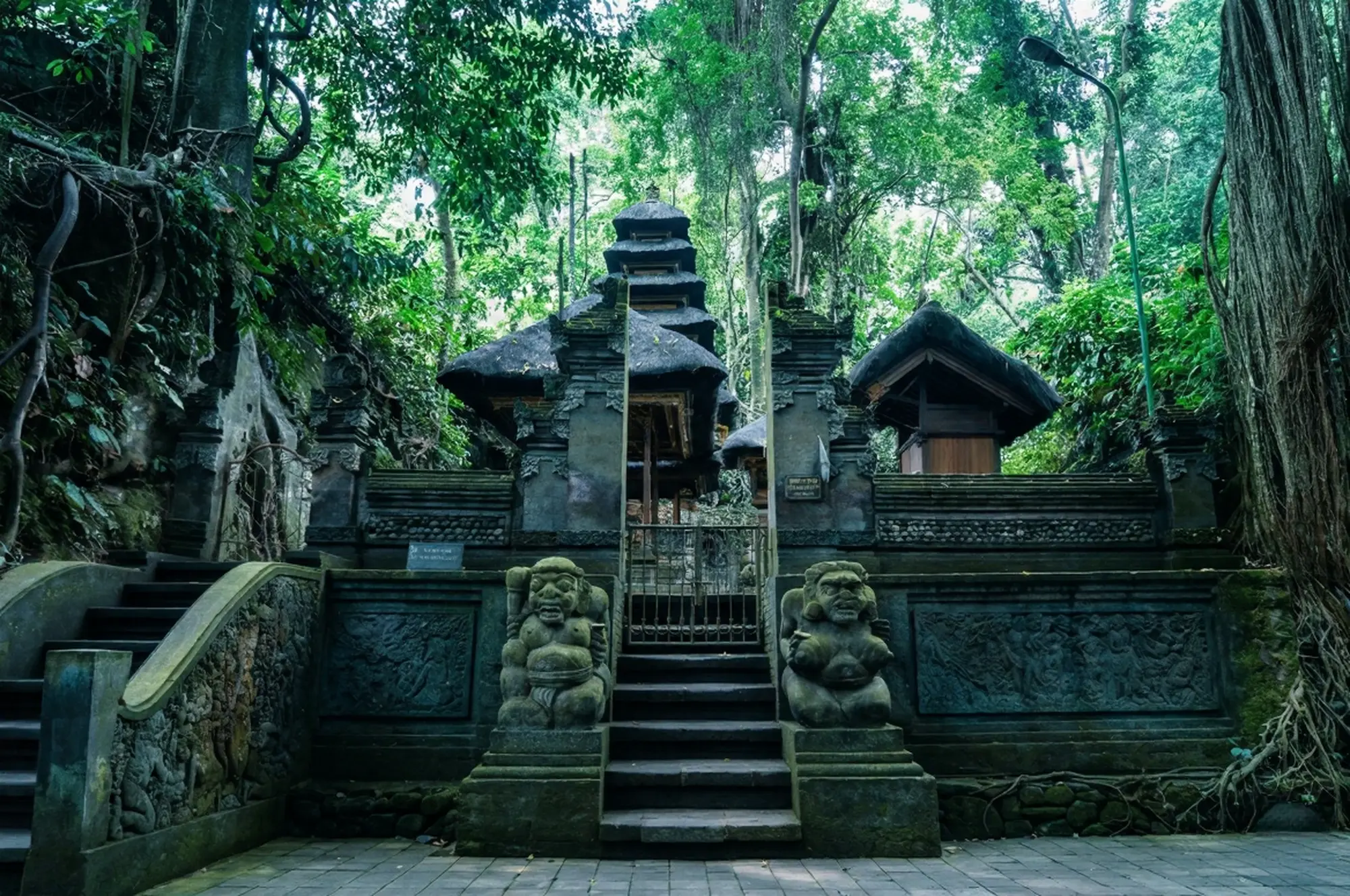 The beautiful moss-covered stone stairs, guardian statues, and entrance gate of Pura Beji, a sacred purification temple hidden deep within Monkey Forest Ubud.