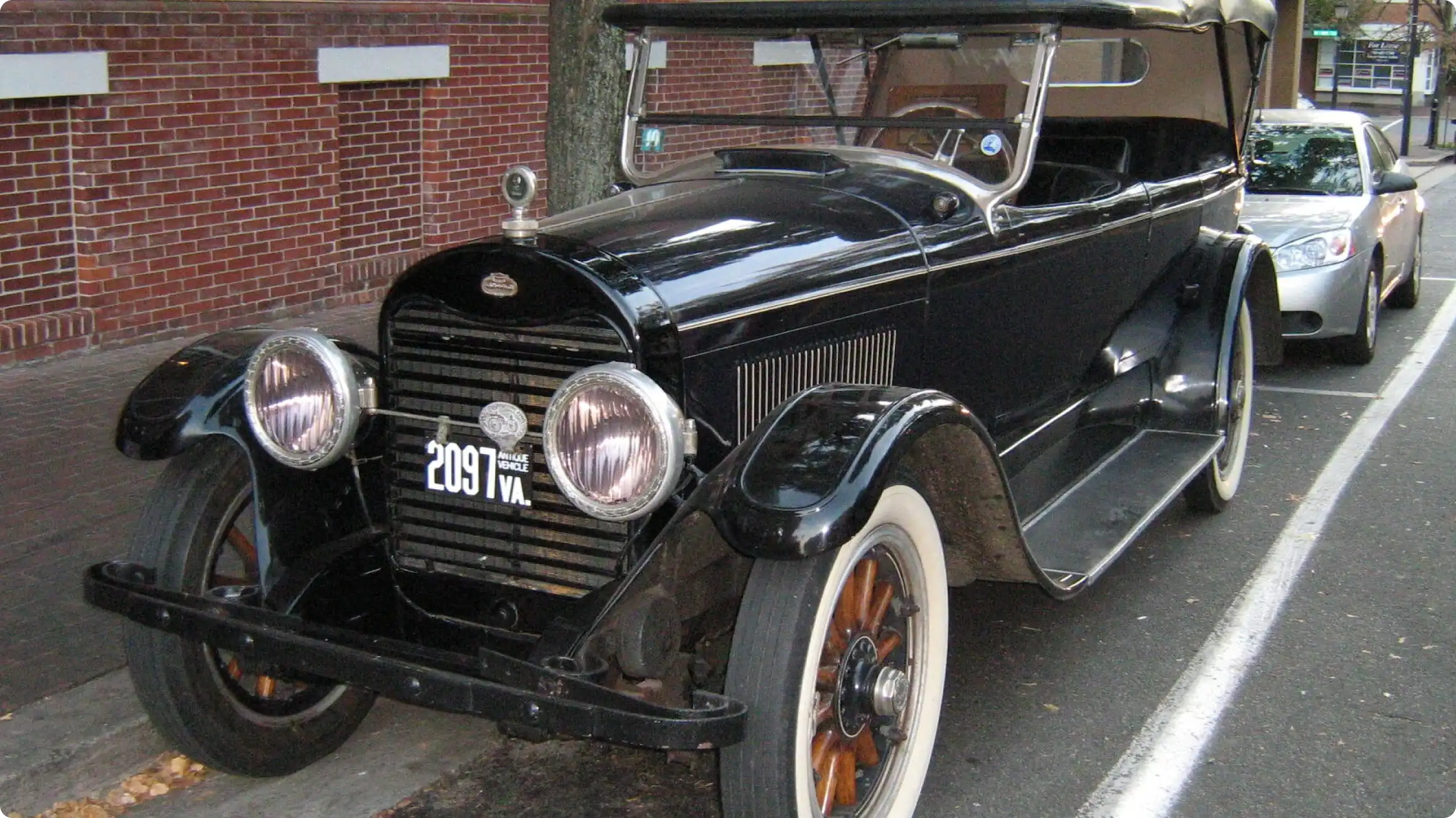 Ретро-автомобиль Lincoln 1920-х годов с черным кузовом, круглыми фарами и деревянными спицами колес, припаркованный на городской улице.