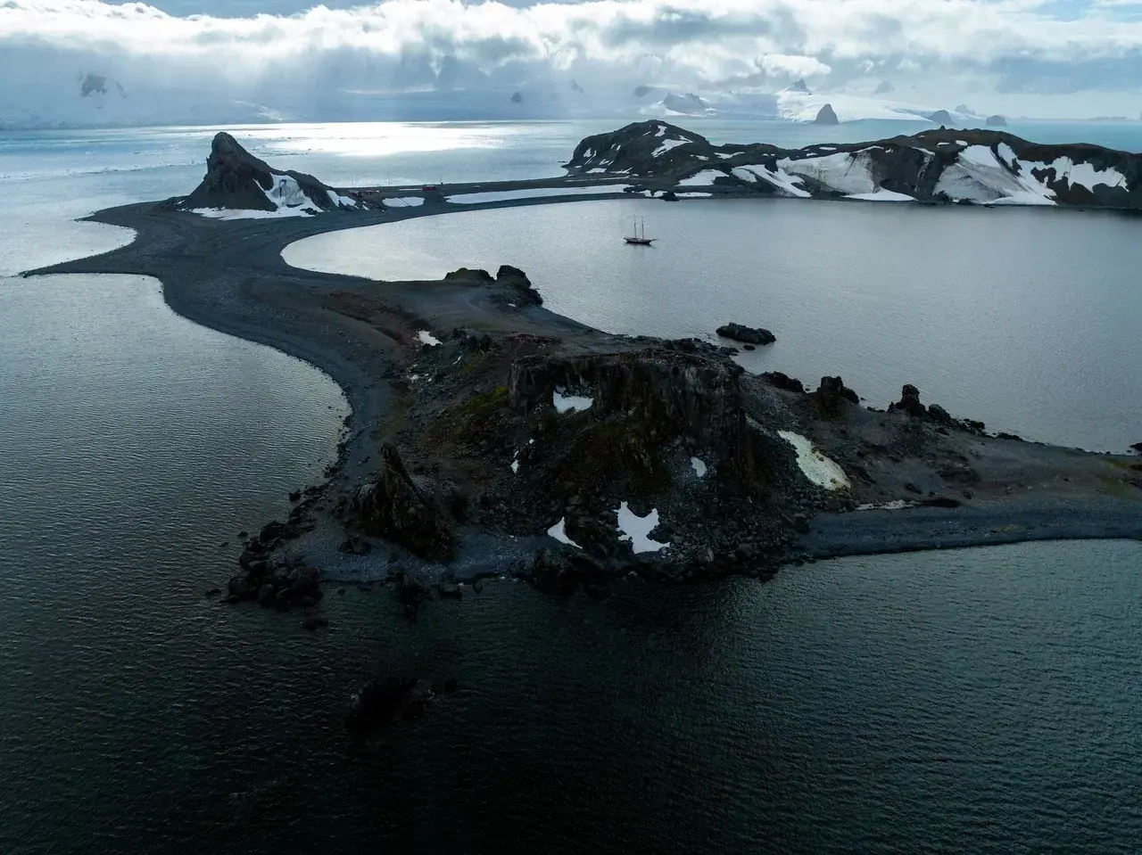 Sailing yacht anchored in a remote volcanic bay surrounded by snow-covered mountains during an Antarctica expedition.