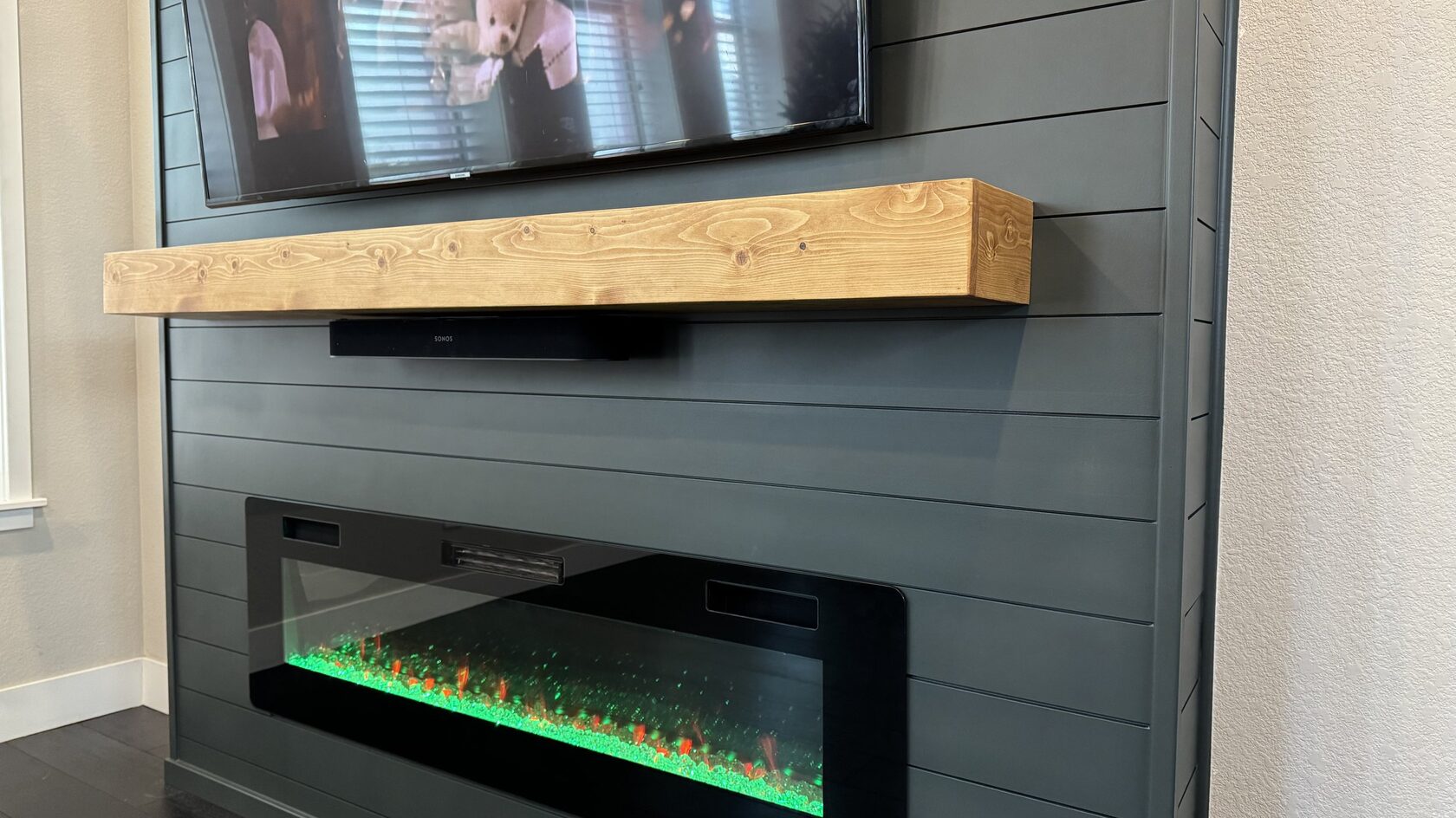 Close-up of the wood mantel, soundbar, and dark painted shiplap above the fireplace.