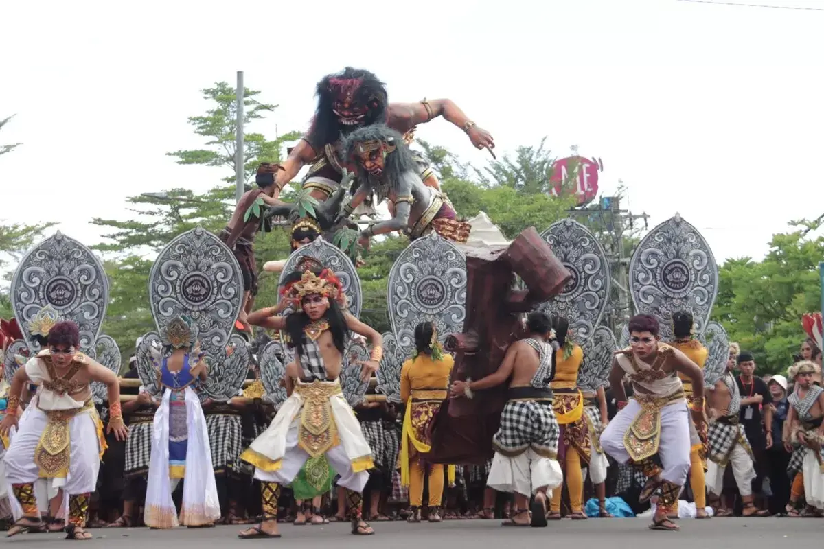 A group of Balinese men in traditional attire energetically carrying and shaking a bamboo platform supporting a monster statue during a daytime Ogoh Ogoh Bali parade.