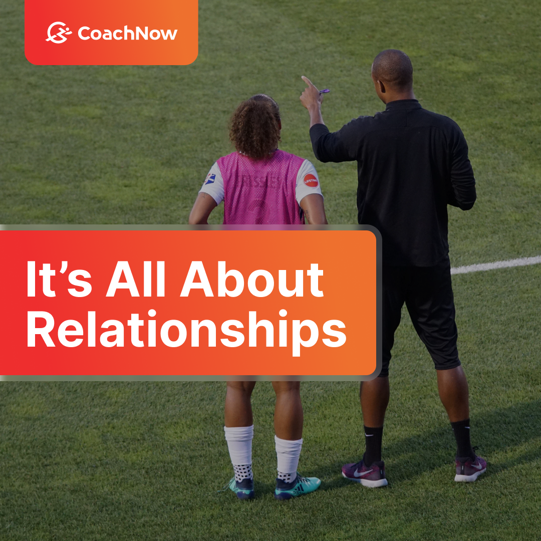CoachNow It's All About Relationships. A coach in an all black outfit speaking to a female soccer athlete wearing a pink jersey, white socks, and teal adidas cleats.