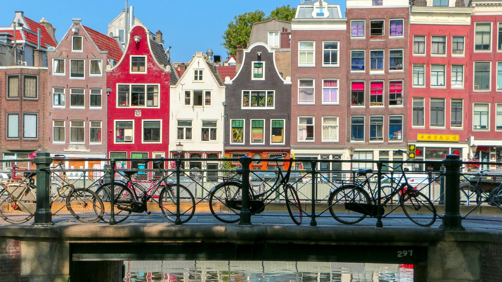 Bicycles parked on a canal bridge in front of tall, colourful Amsterdam canal houses