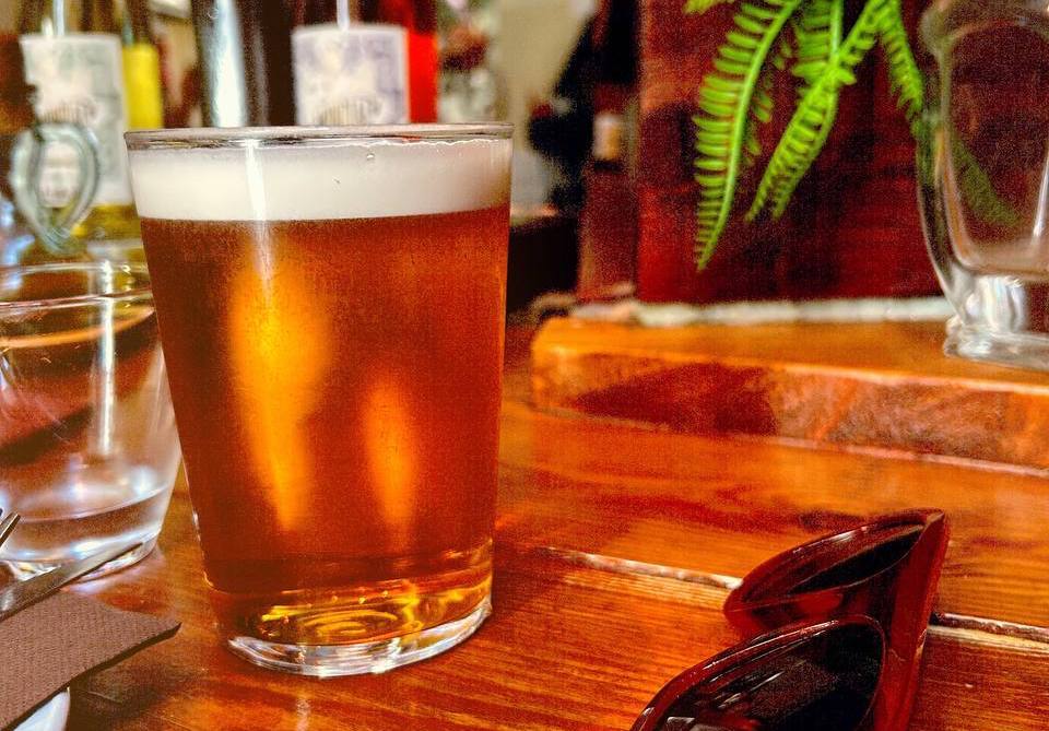 A glass of beer next to sunglasses on a wooden table at Sensi