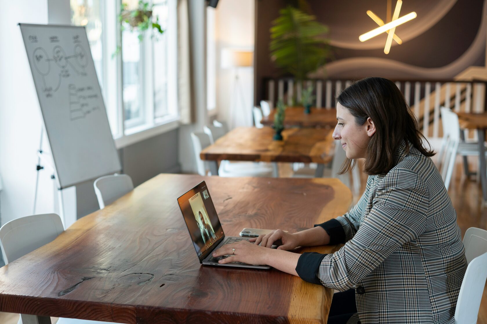 A focused woman sitting at a desk, working on a side project with a laptop and notebook in front of her