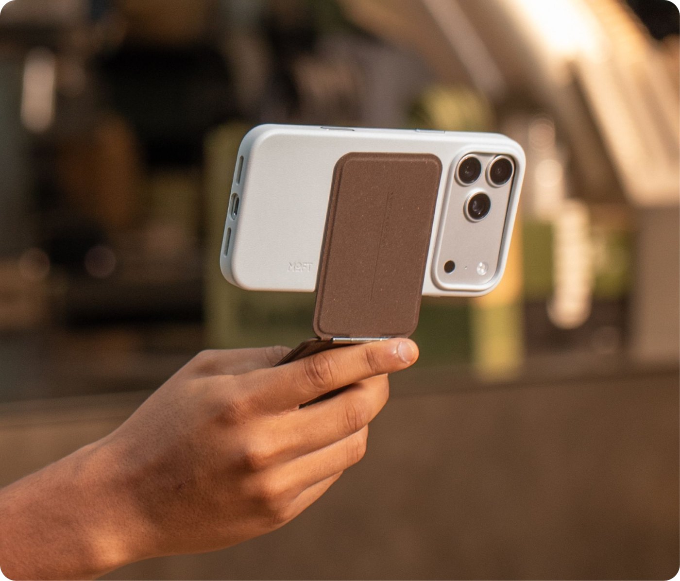 Рука держит iPhone за сложенную подставку MOVAS-E