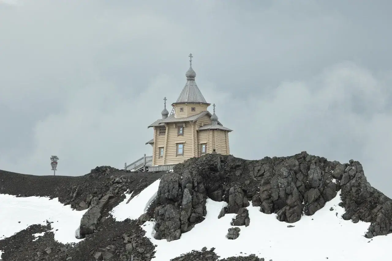 Holy Trinity Church on King George Island the southernmost Orthodox church on Earth standing atop a volcanic ridge overlooking Antarcticas dramatic landscape. Its traditional wooden architecture contrasts beautifully with the surrounding snow dark volcani