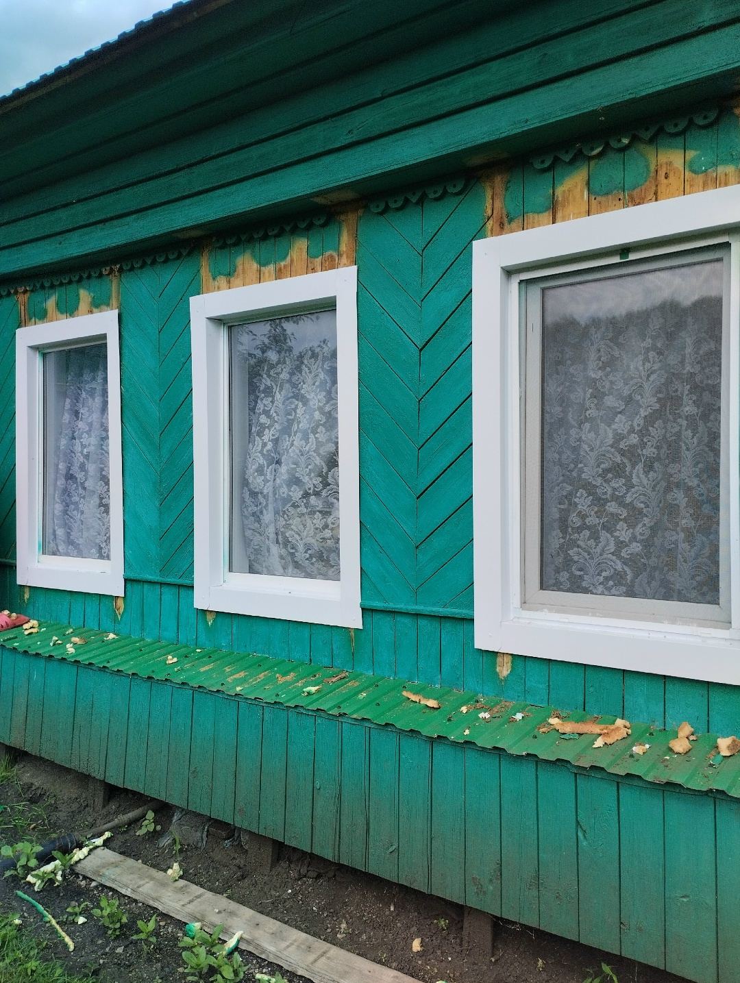 Три белых окна на фасаде зелёного деревянного дома