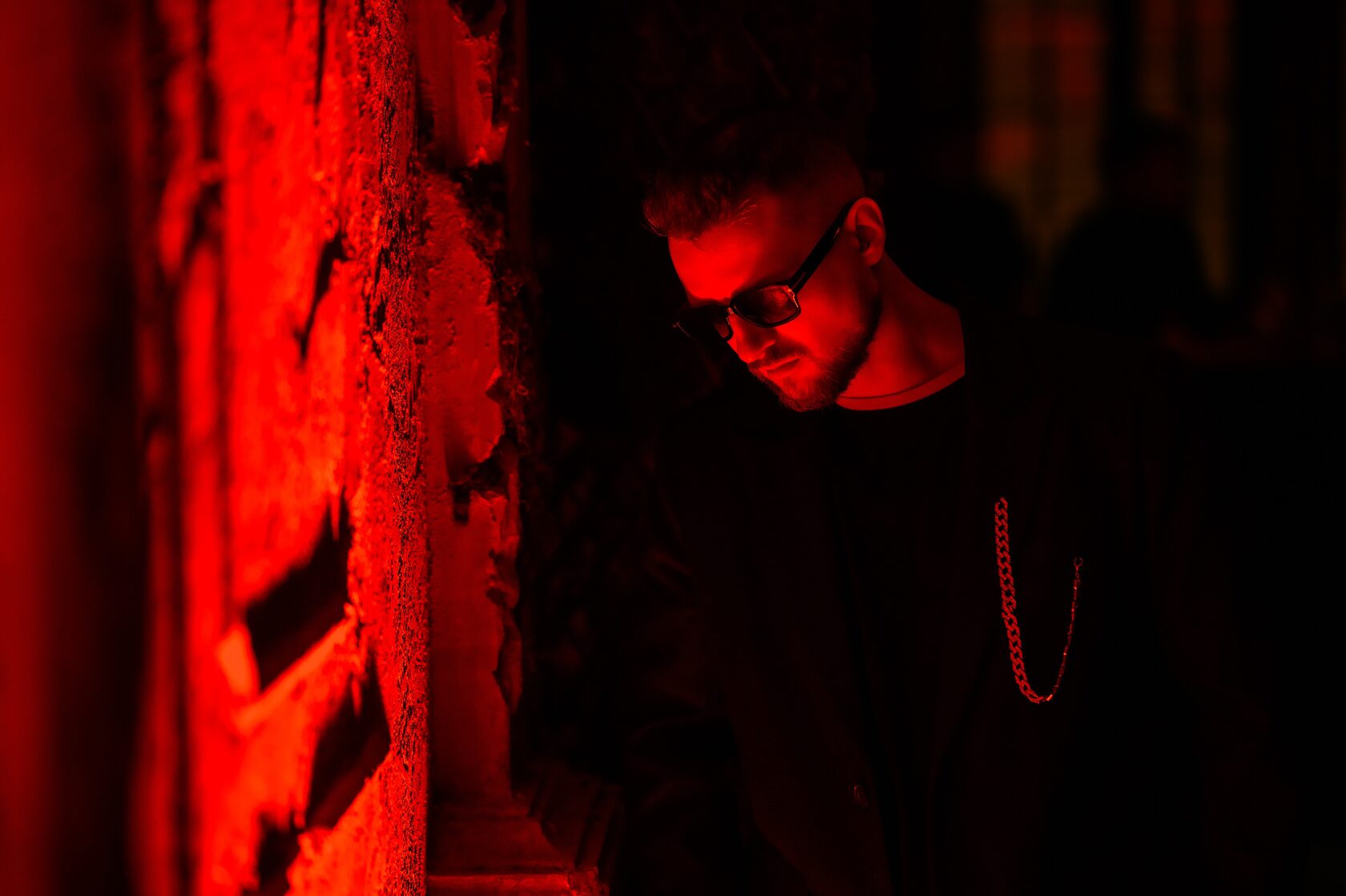 Портрет DJ ROZHKOV в чёрной одежде и тёмных очках у стены с красной подсветкой.