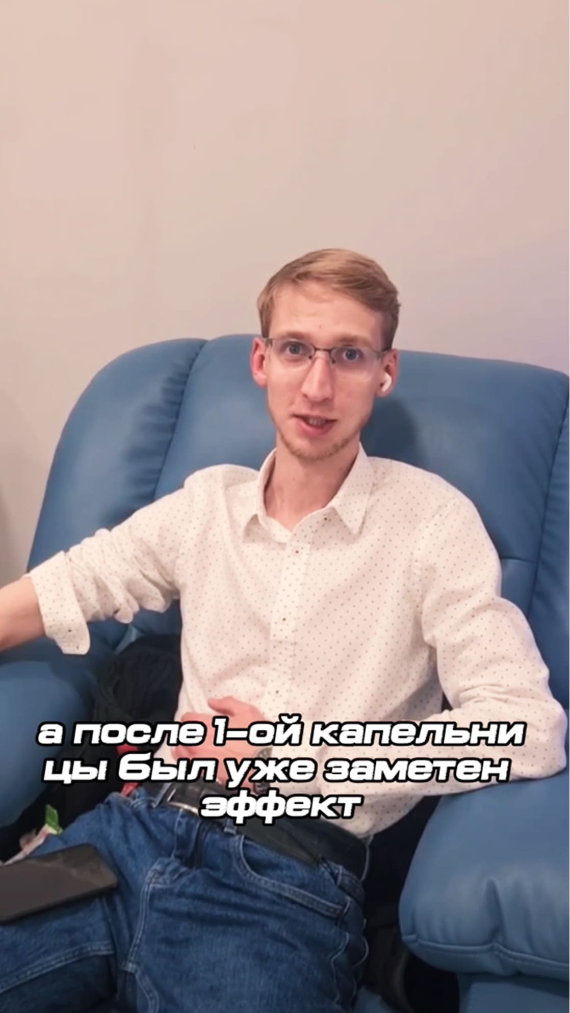 Молодой мужчина в белой рубашке и очках сидит в синем кресле. Субтитр: «а после 1-ой капельницы был уже заметен эффект»