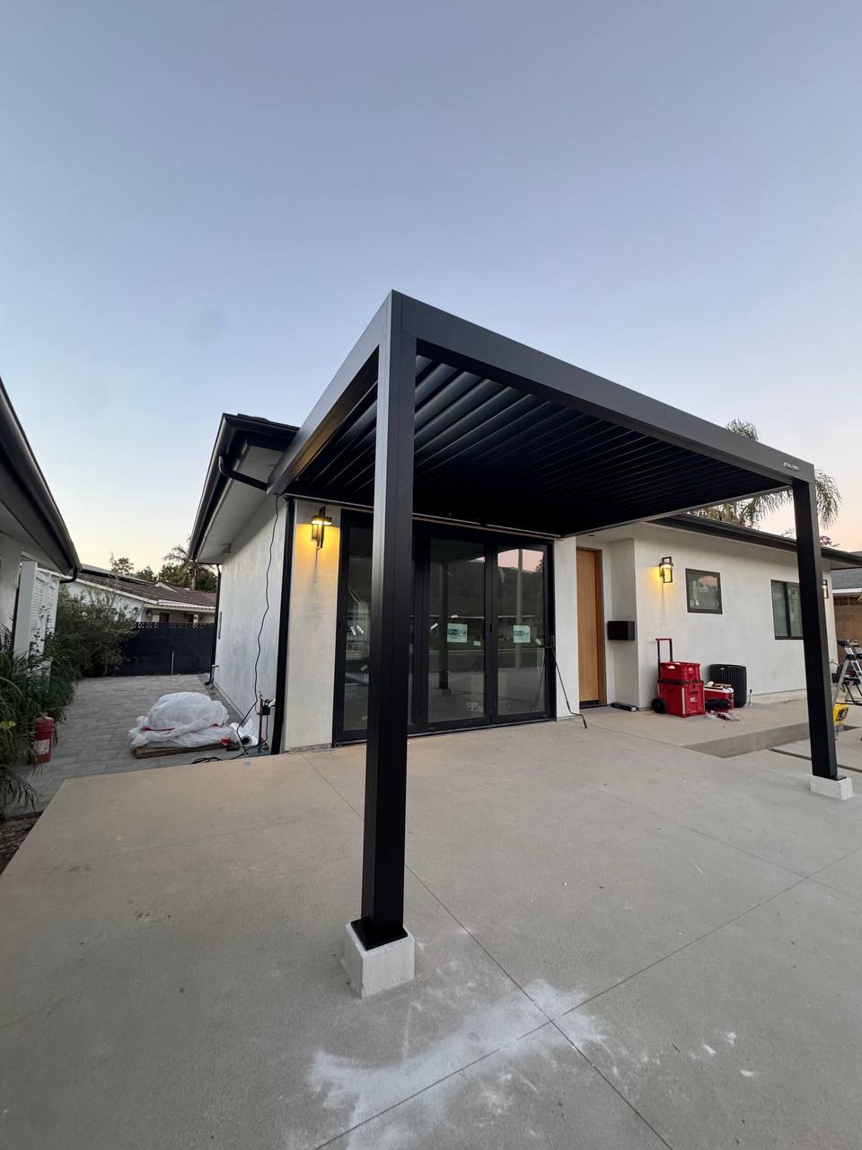 Wide side-yard view of the completed black pergola beside the house.