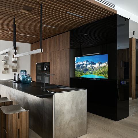 Встроенный телевизор Теле-Арт за чёрным стеклом от пола до потолка на кухне с островом. Глянцевая поверхность объединяет интерьер и скрывает технику.