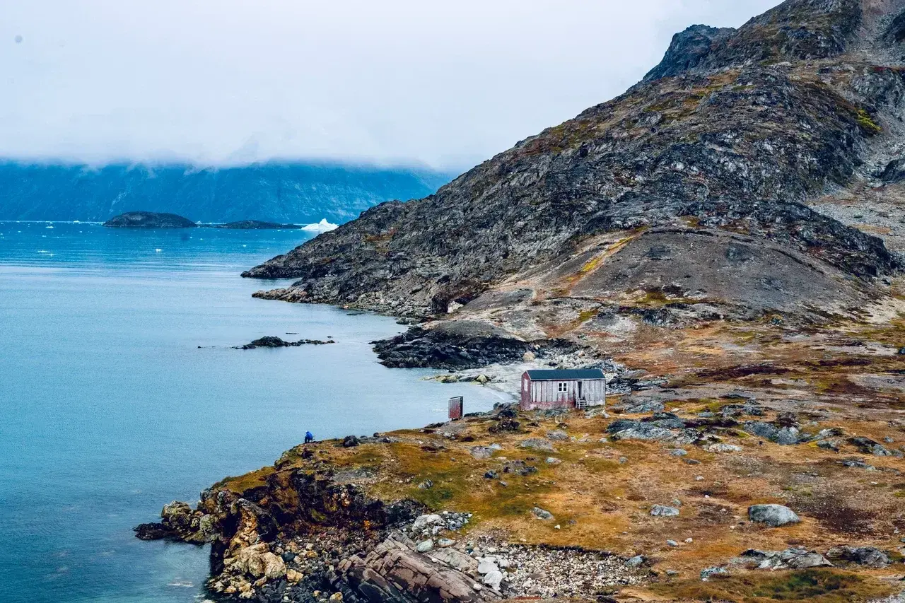 Isolated Greenland cabin beside an Arctic fjord with dramatic mountains, remote wilderness, and polar landscapes
