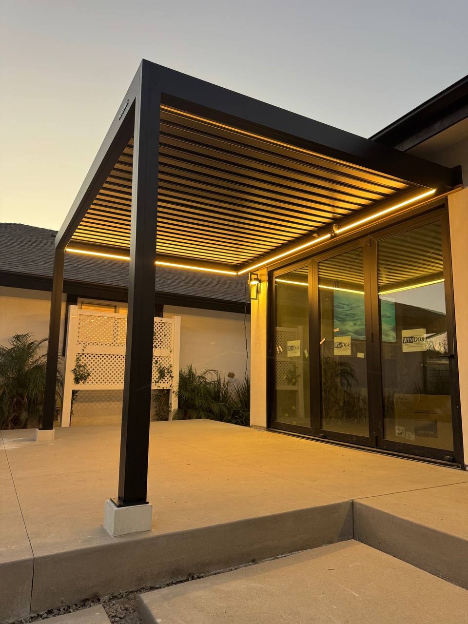 Low-angle view of the black pergola roof and warm LED lighting in the evening.