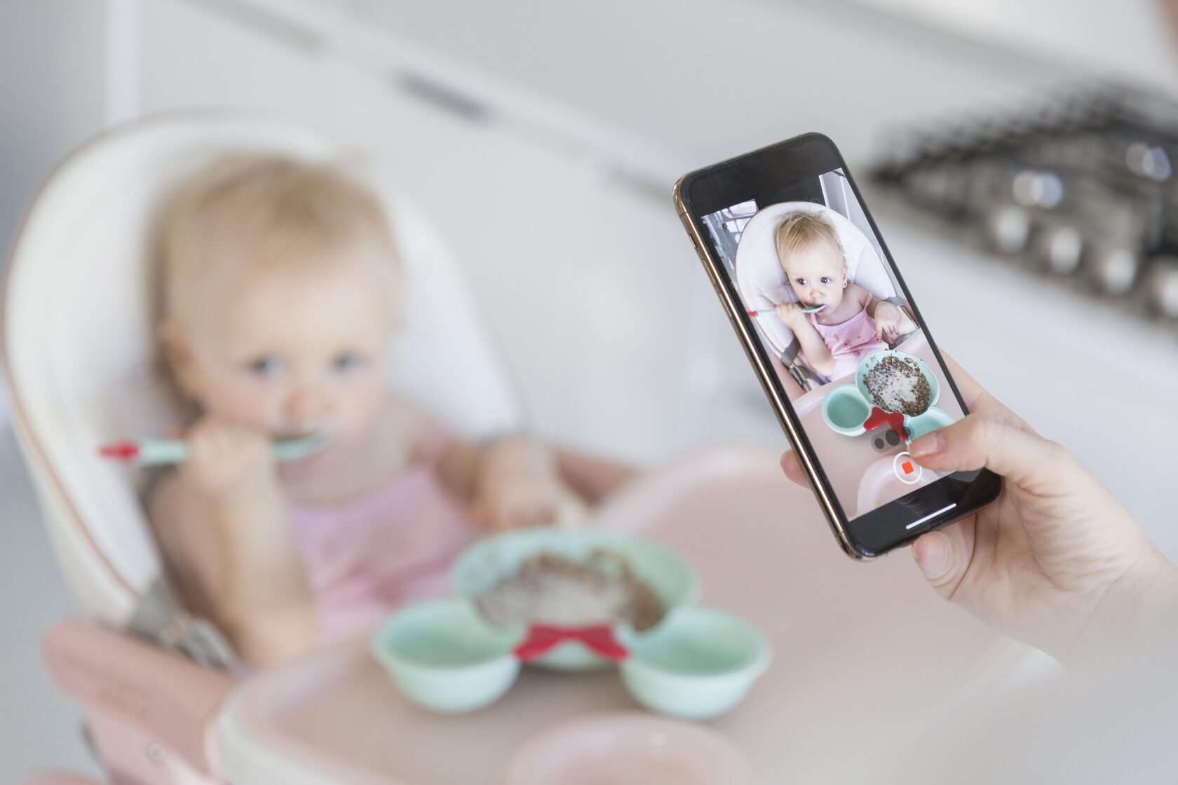 Baby eating solid food with parent recording feeding information in a baby tracking app on a smartphone.