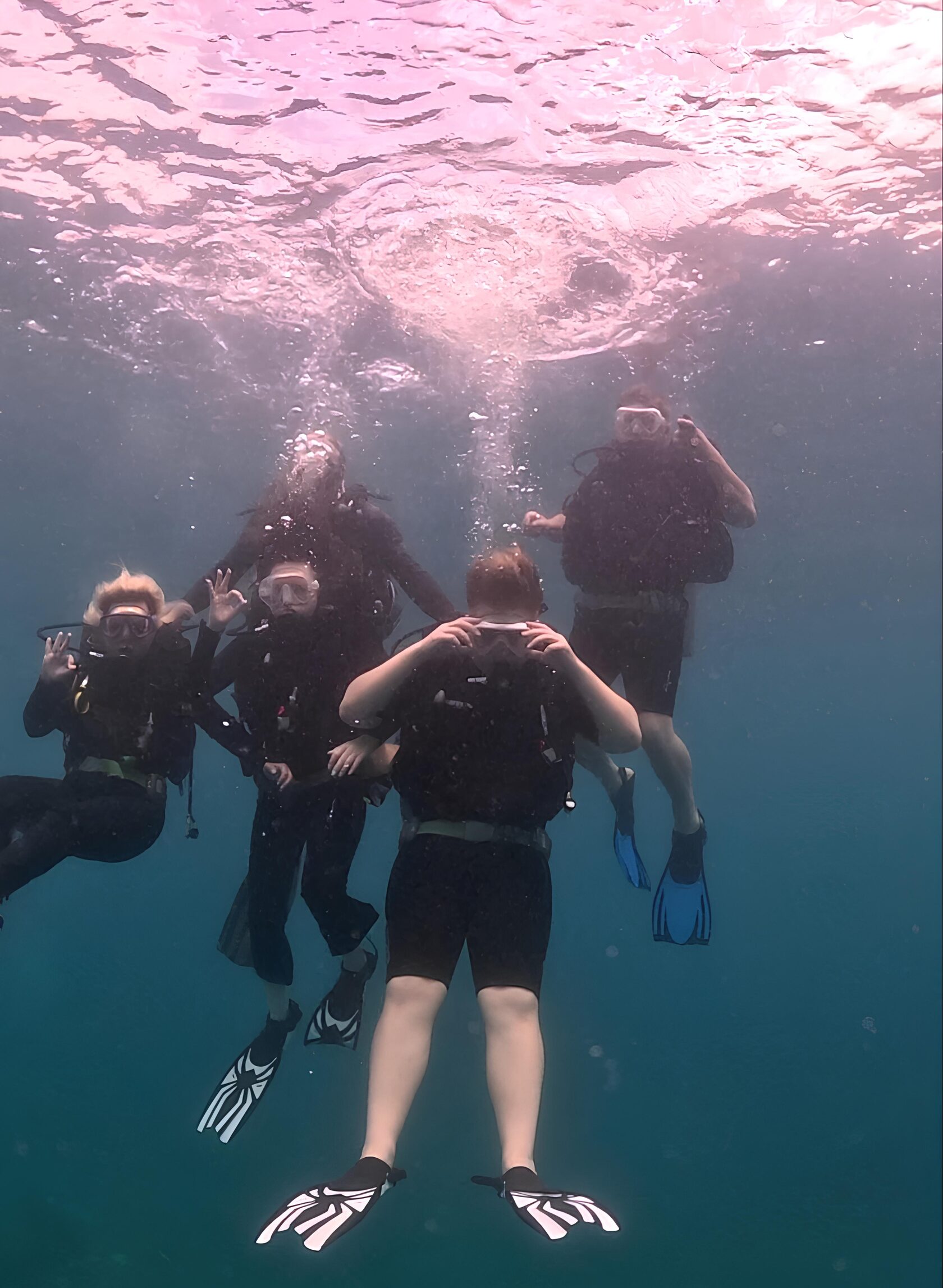 Семья из четырех человек занимается дайвингом в чистых водах Южно-Китайского моря на побережье курорта Нячанг, дайверы в снаряжении под водой, за ними инструтор в снаряжении помогает им держаться на одном уровне