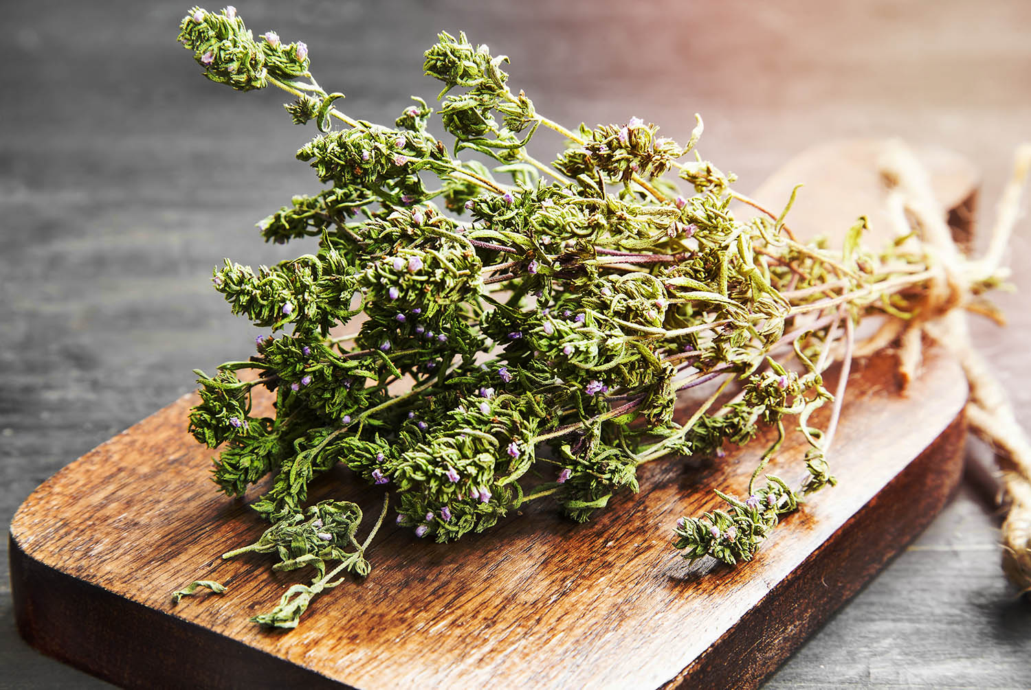Dried thyme bundle with purple flowers on a wooden cutting board, highlighting Mediterranean herbs for gardening tips on growing lavender, thyme, and oregano together.