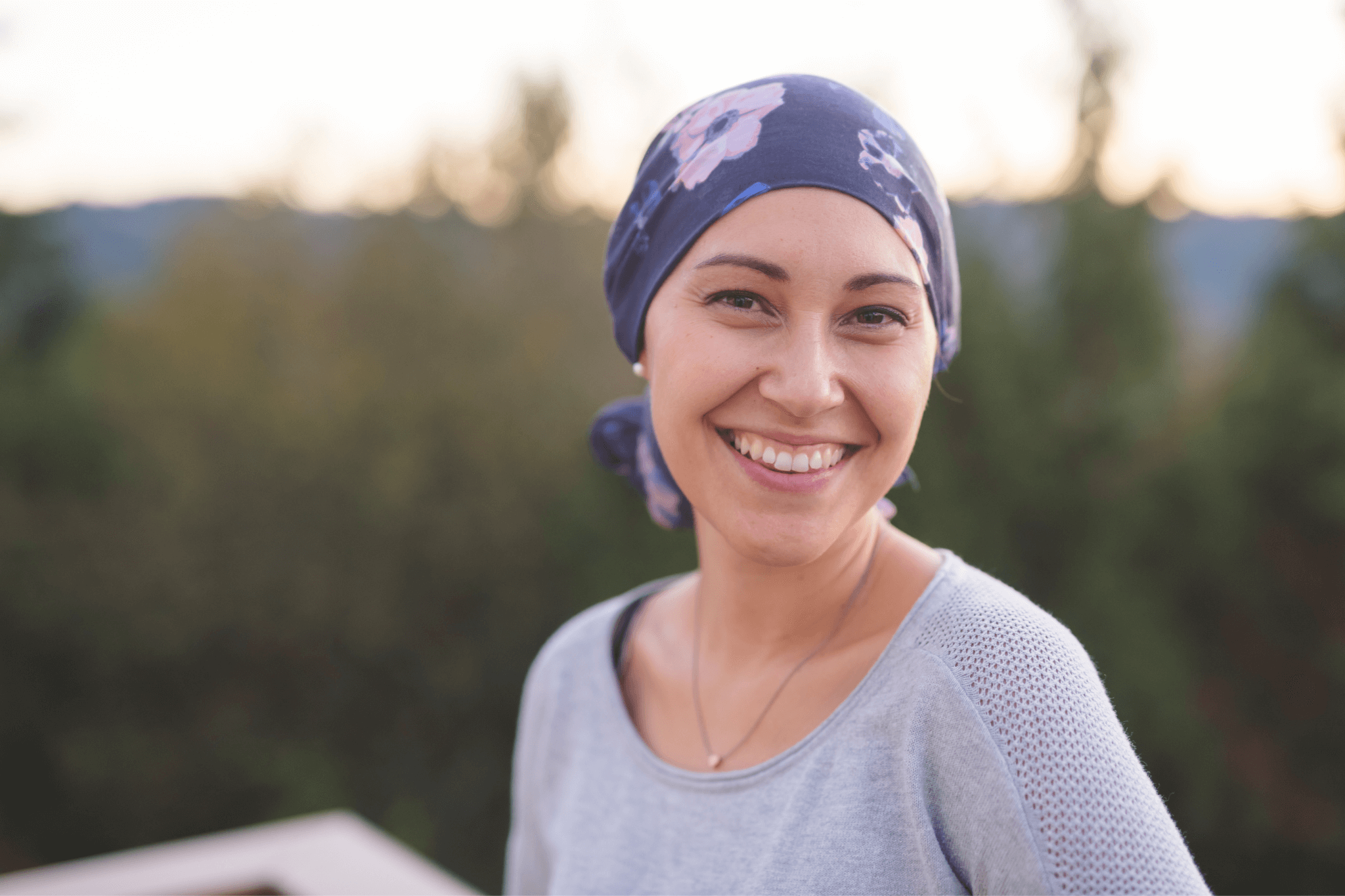 Lächelnde Tumorpatientin mit blauem Kopftuch auf Balkon