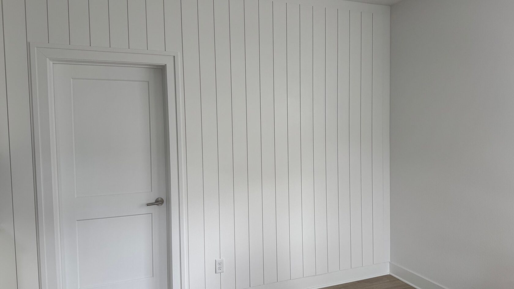 Vertical white shiplap accent wall with doorway casing and baseboard detail.