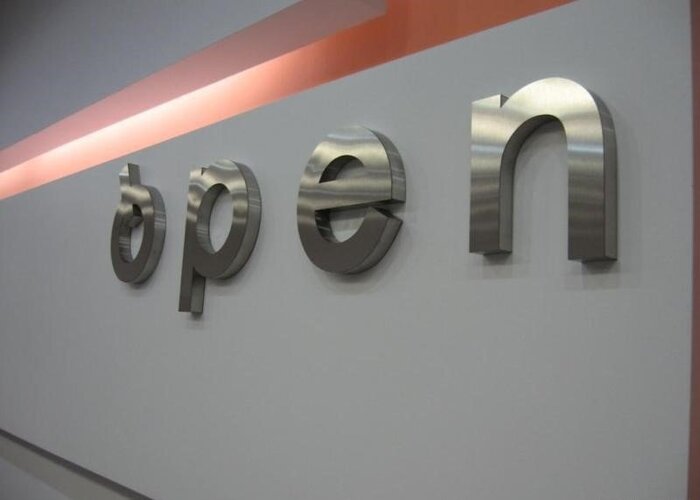 Шлифованные объёмные буквы open на серой стене в интерьере