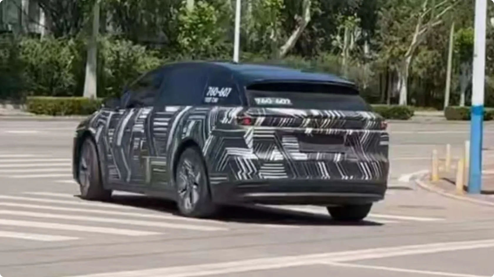 Шпионское фото тестового прототипа Li Auto i6 в камуфляже, движущегося по городской улице: скрытые линии кузова, черная крыша и характерная задняя светодиодная полоса.