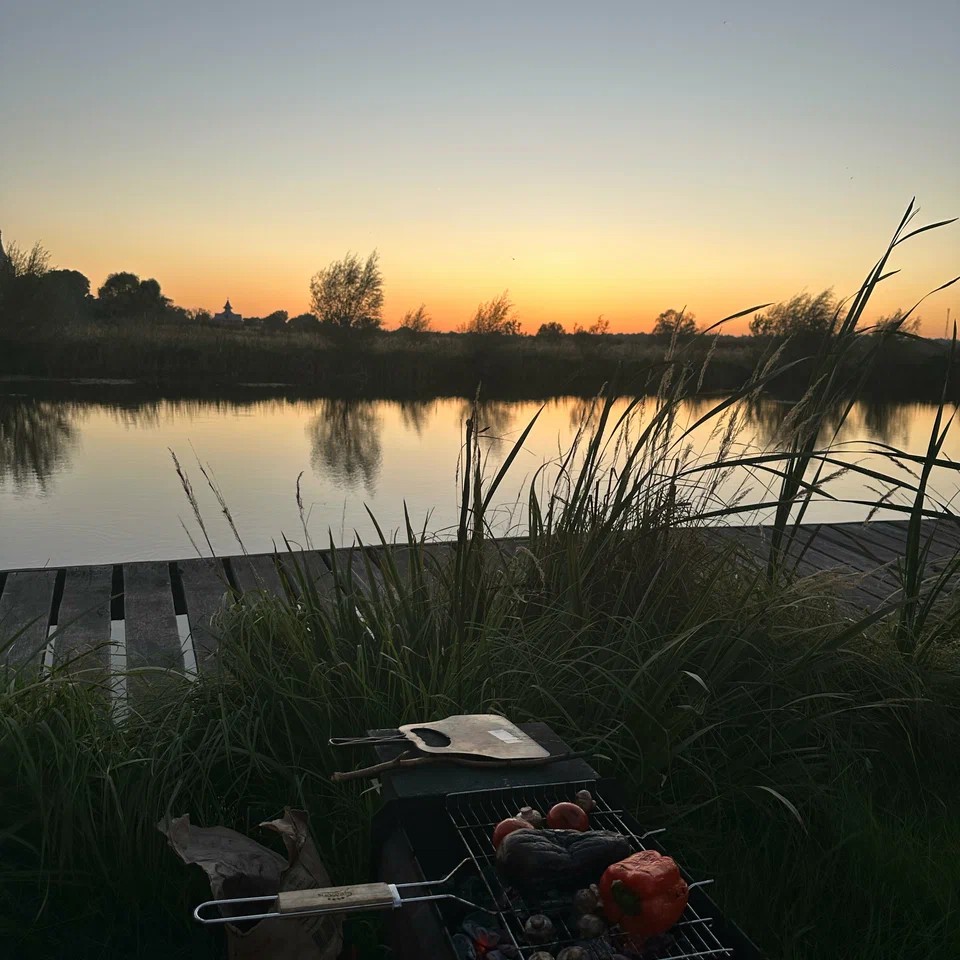 A mangal with glowing coals grilling dinner by the water at sunset