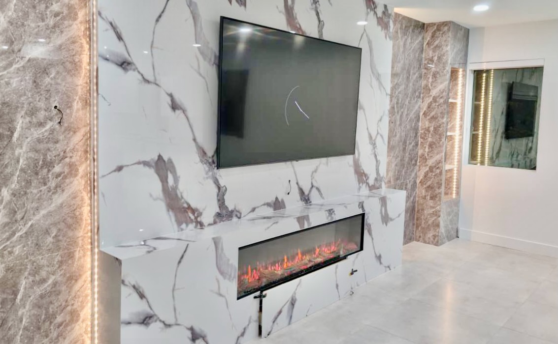 Custom media wall featuring a mounted TV, long electric fireplace, marble-look decorative panels, and warm vertical LED lighting.