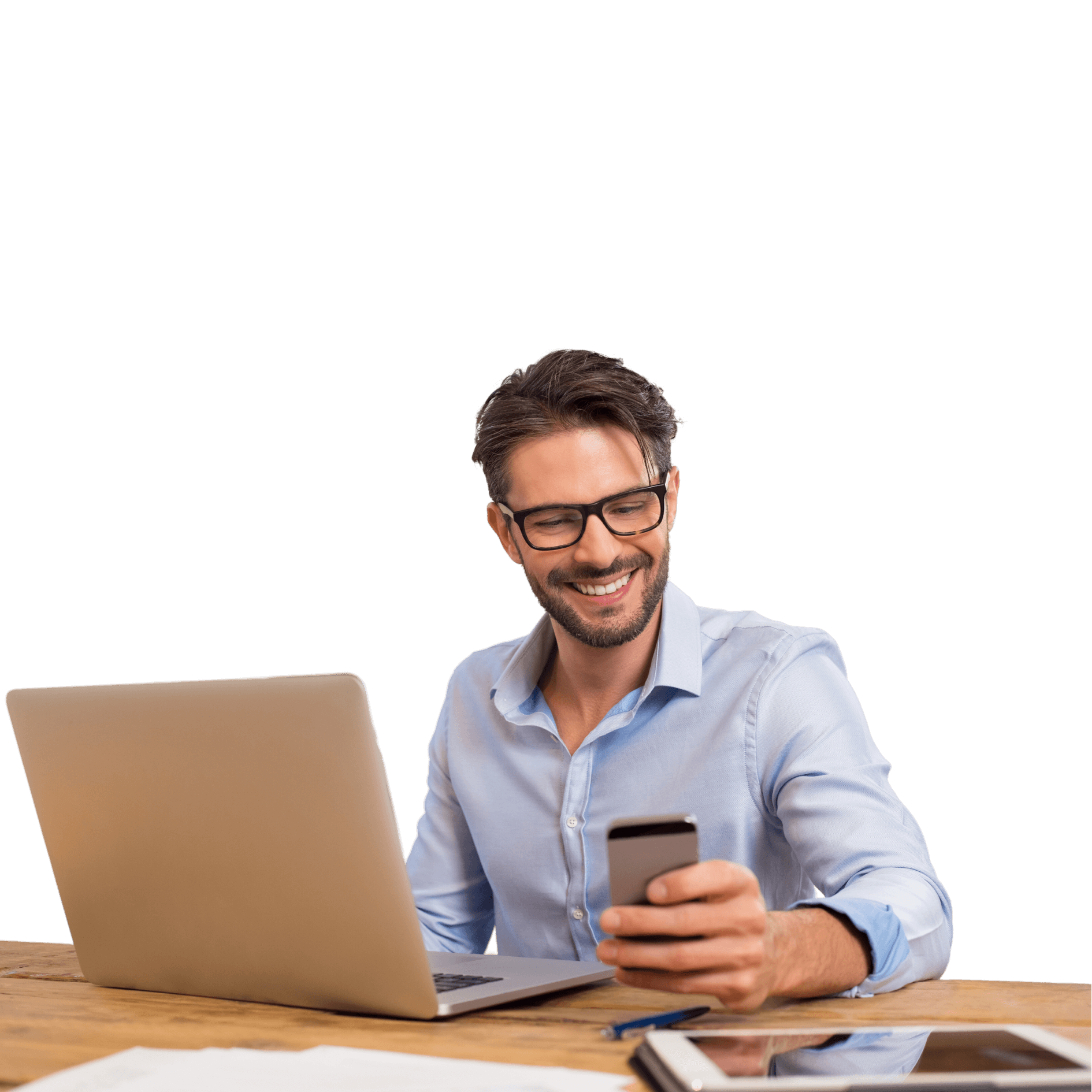 Улыбающийся мужчина в очках, сидящий за столом зак компьютером и телефоном в руках.