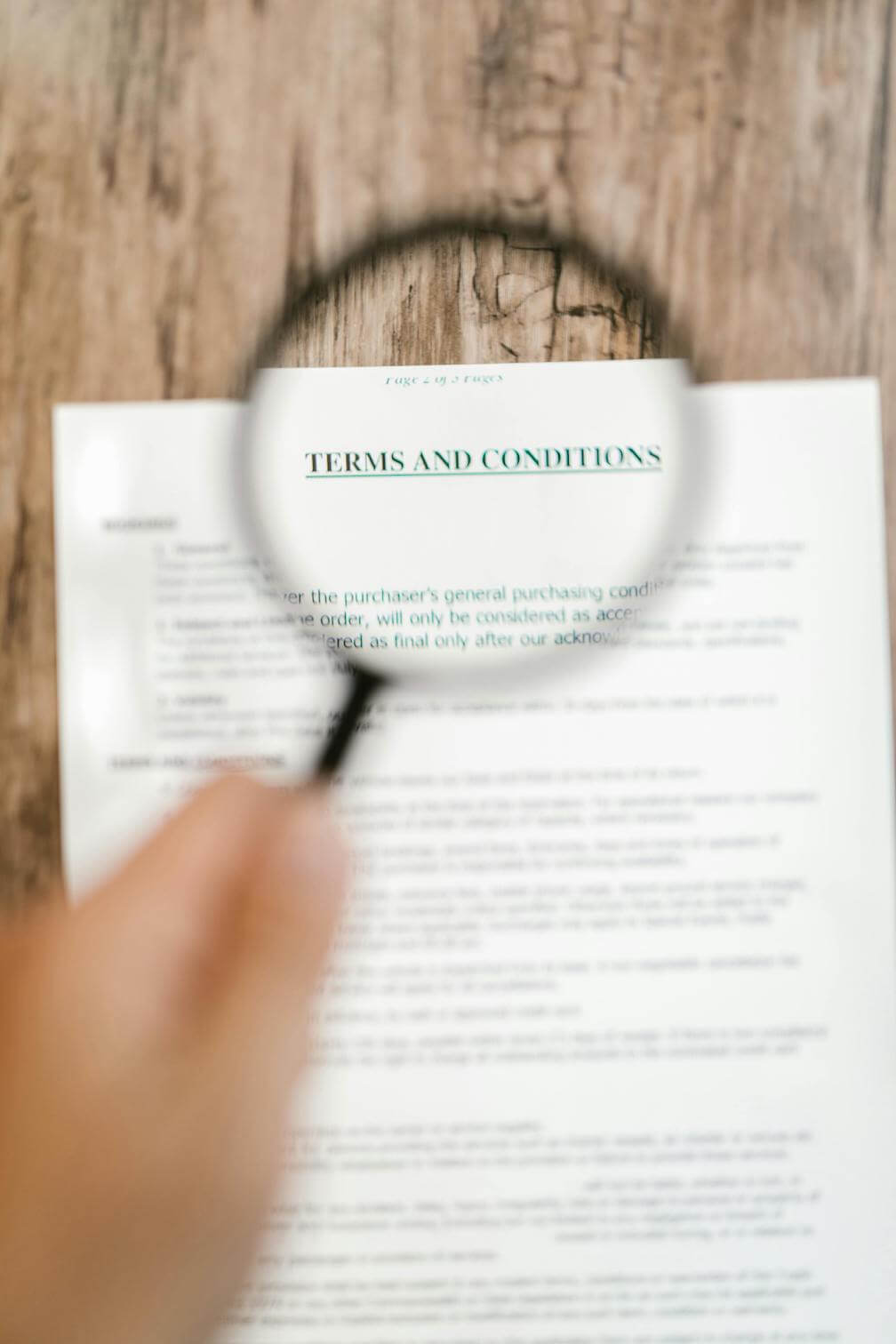 A hand holds a magnifying glass over a document with the words “special conditions” visible.