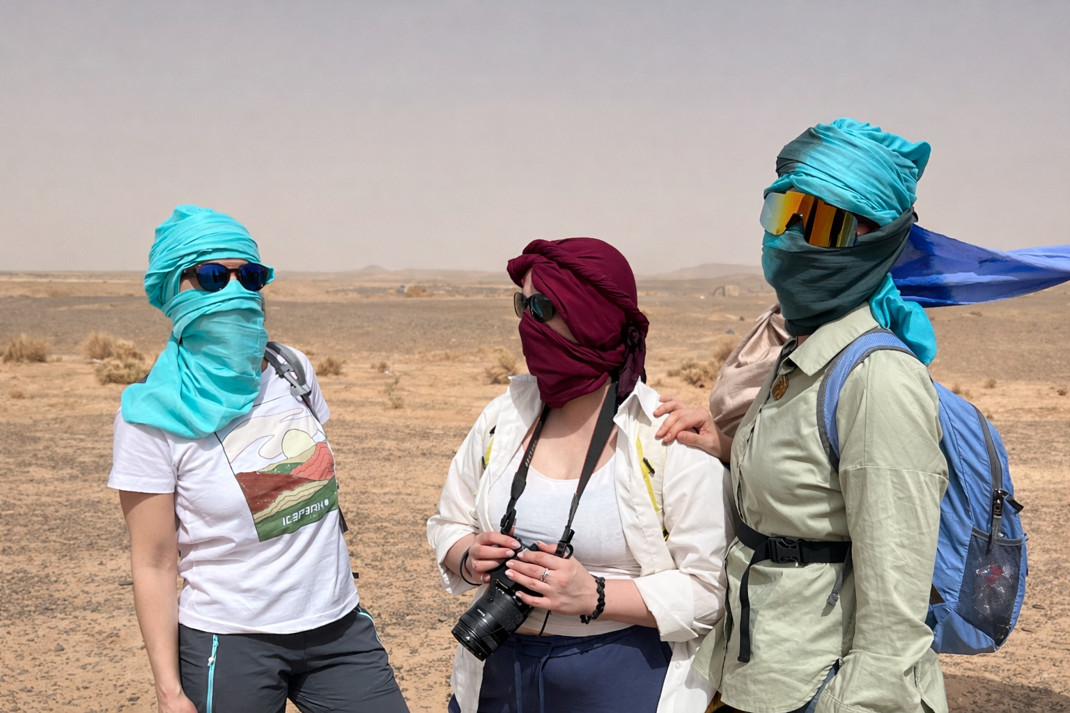three people in Sahara desert wearing traditional scarves during fossil hunting expedition