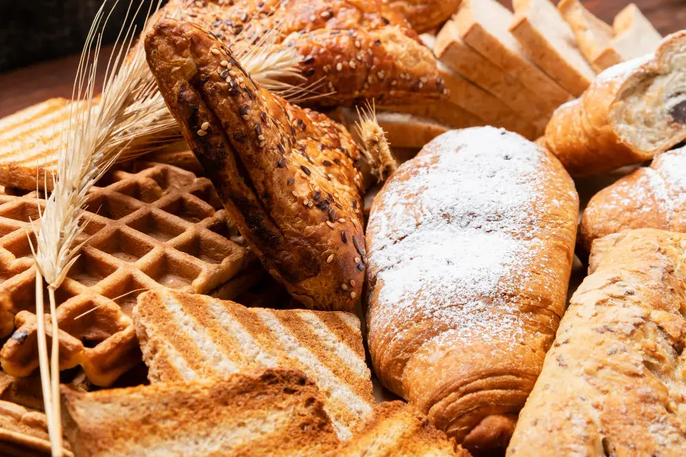 Разнообразная выпечка из пшеничной муки: хлеб, круассаны и вафли — визуализация чрезмерного потребления глютена в современном рационе.