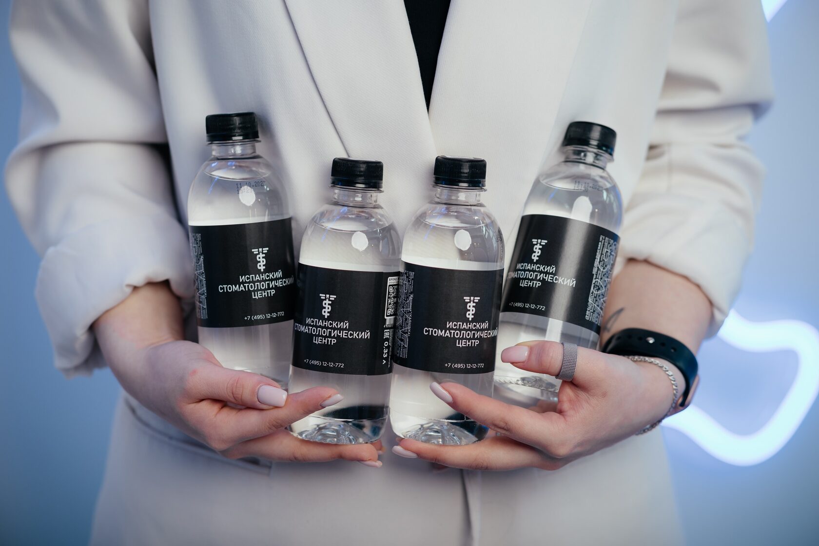 фото на котором две руки девушки держат четыре бутылки с водой с надписью Испанский стоматологический центр