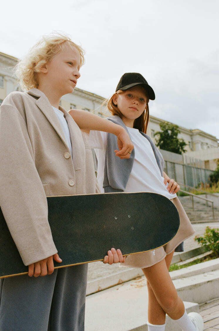 мальчик со скейтом в бежевом пиджаке и серых штанах