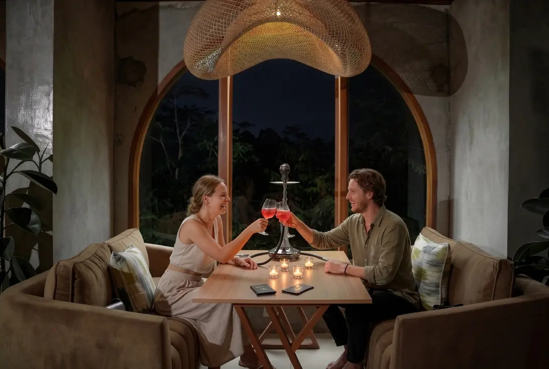 A couple laughing and toasting with colorful cocktails over a smooth shisha setup, capturing the relaxing evening vibe of the best places in Bali for a first date.