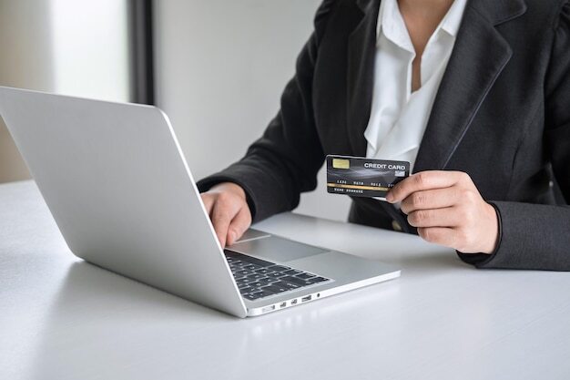 Midsection of woman using laptop while holding credit card on table