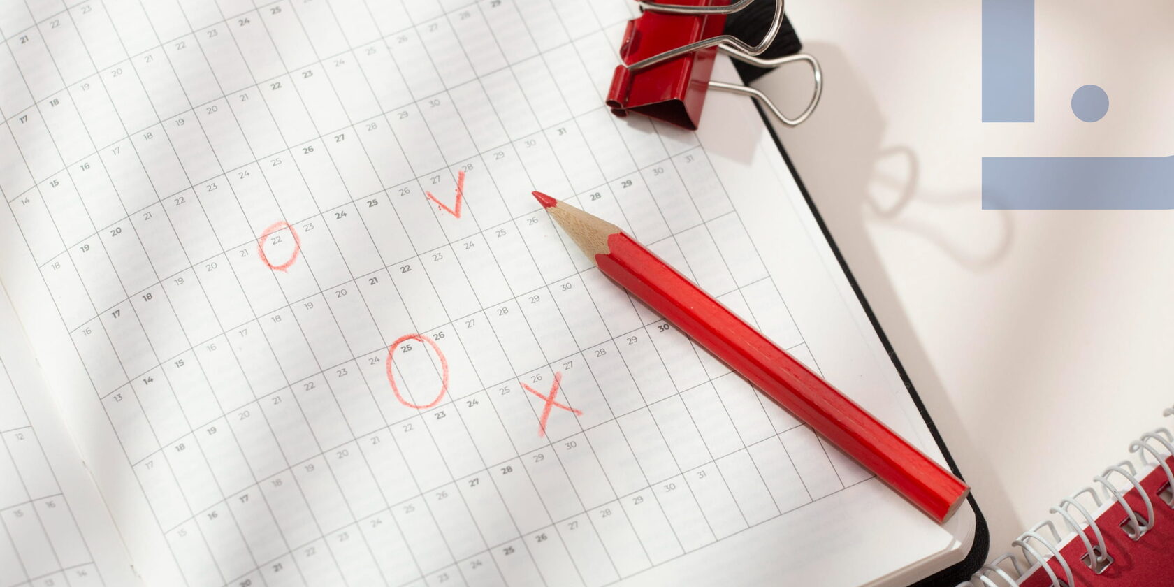 Calendar with markings, a red pencil and office supplies symbolizing task planning, priority setting and workload management.