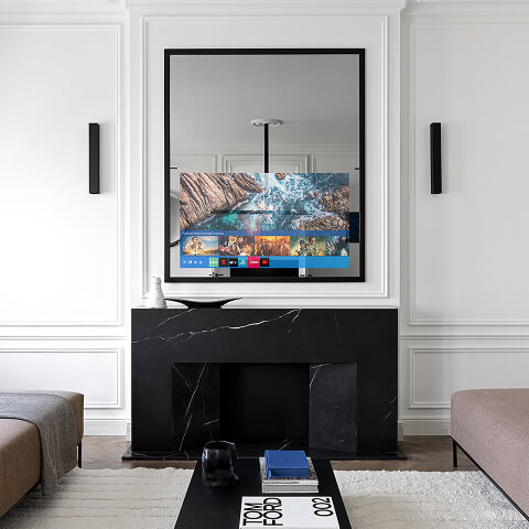 Зеркальный телевизор Теле-Арт над чёрным декоративным камином в светлой гостиной. Экран встроен в зеркало с багетом — техника скрыта.