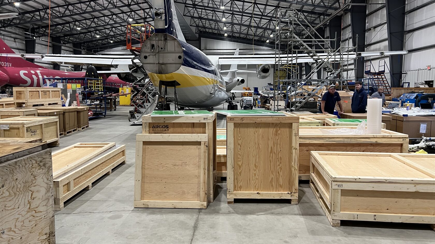 Argos Crating team building a custom ATA-300 crate on-site at an aircraft hangar — ISPM-15 certified lumber used as standard for all international shipments