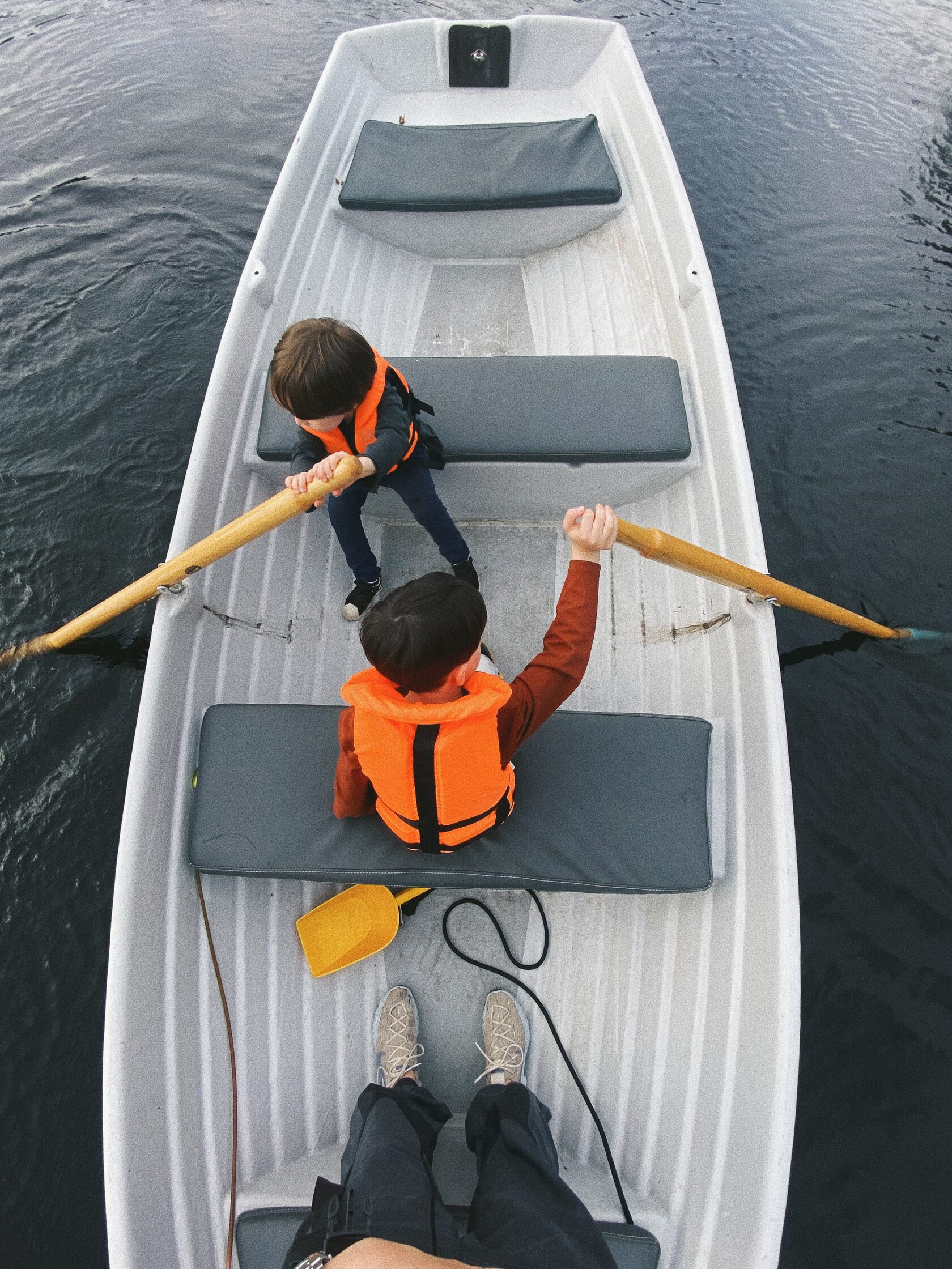 дети в оранжевых жилетах гребут в лодке