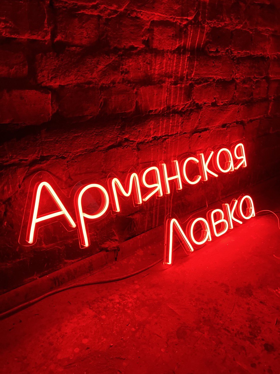 Красная неоновая вывеска «Армянская лавка» на кирпичной стене магазина