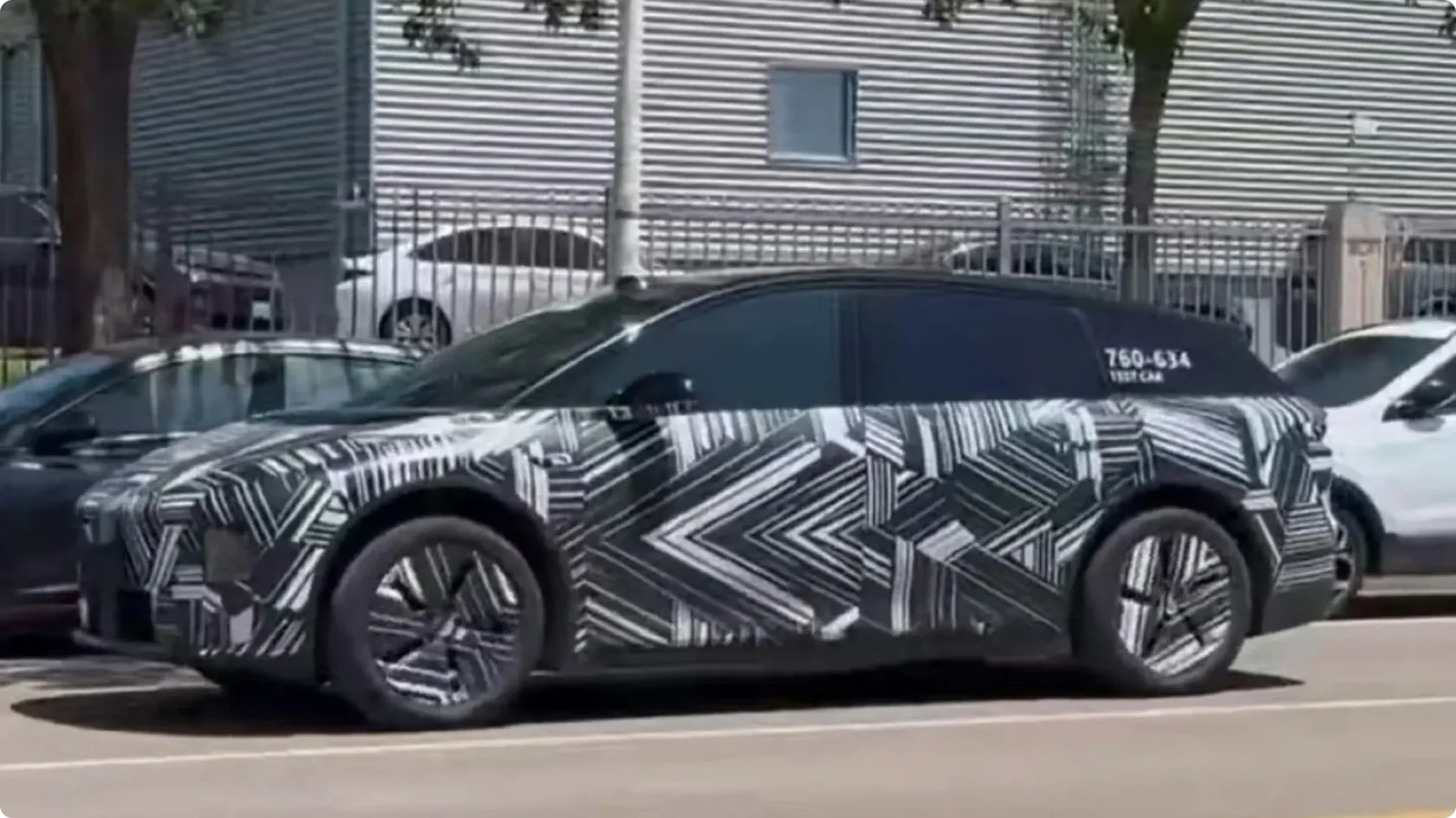 Боковой профиль закамуфлированного прототипа Li Auto i6 на городской улице: обтекаемый кузов, парящая черная крыша и аэродинамические диски с маркировкой тестового автомобиля.