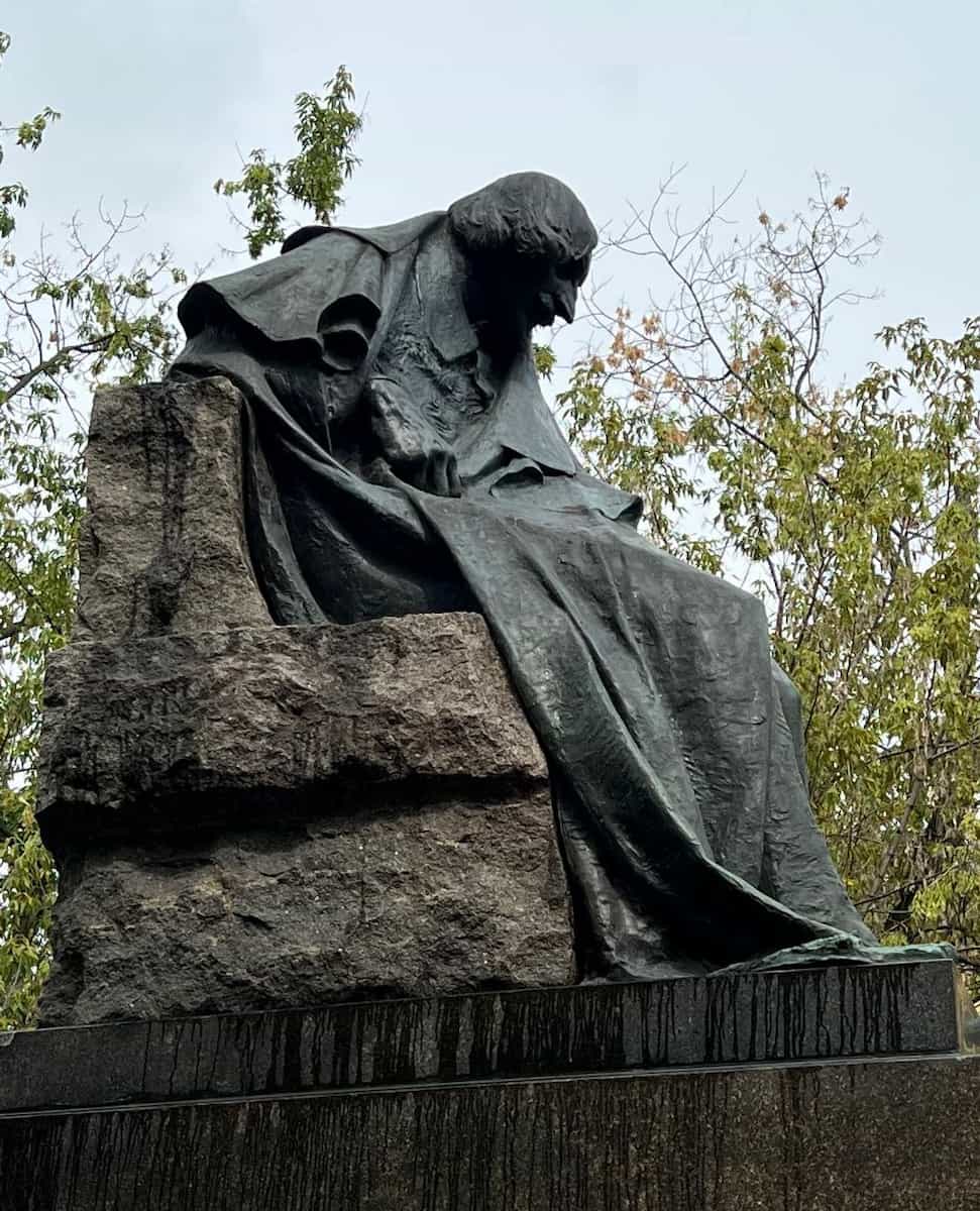 Памятник Николаю Гоголю на каменном постаменте среди деревьев