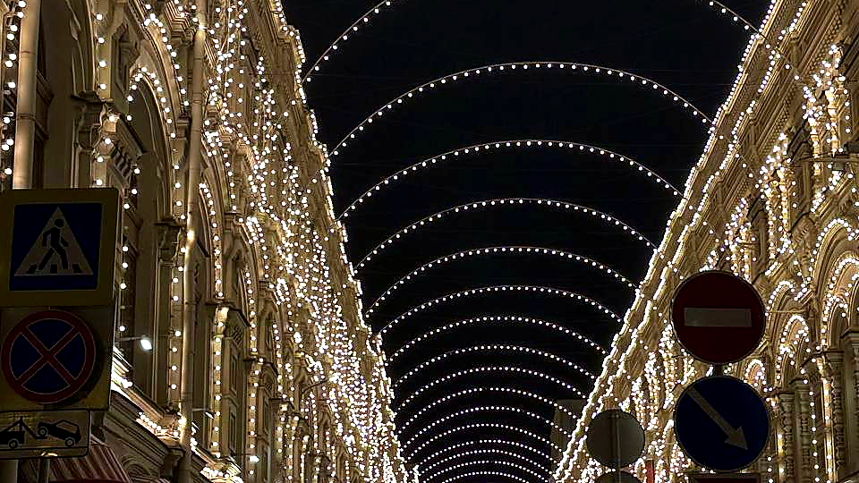 Ночной фасад исторического здания с праздничной иллюминацией и световыми арками над улицей — атмосфера зимнего вечера и городского события.